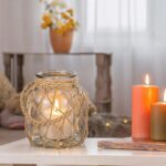 Two clear glass nautical lanterns with jute rope handles and flickering LED candles inside, on a tabletop.